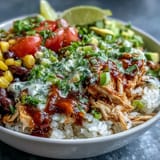 Tender shredded chicken simmered in zesty salsa, layered with rice and vibrant toppings like cherry tomatoes and cilantro.  