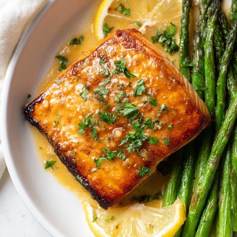 Skillet Lemon-Butter Salmon, glistening with lemon sauce, served over tender asparagus for dinner.