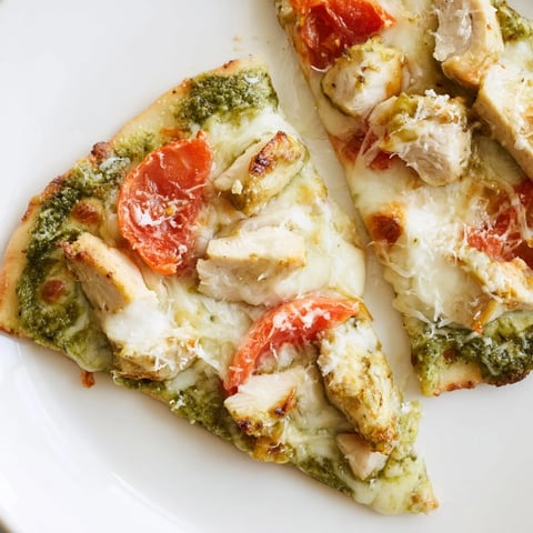 Golden-brown Chicken Pesto Pizza emerges from the oven, featuring melted mozzarella, vibrant tomato slices, and fresh basil garnish.  