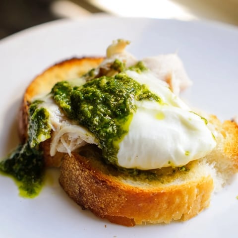 Crispy sourdough toast topped with tender chicken, basil pesto, and creamy burrata, garnished with fresh basil leaves.  