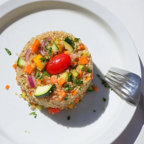 Fluffy quinoa vegetable pilaf loaded with roasted red bell pepper, zucchini, and carrots, garnished with fresh parsley and lemon.  