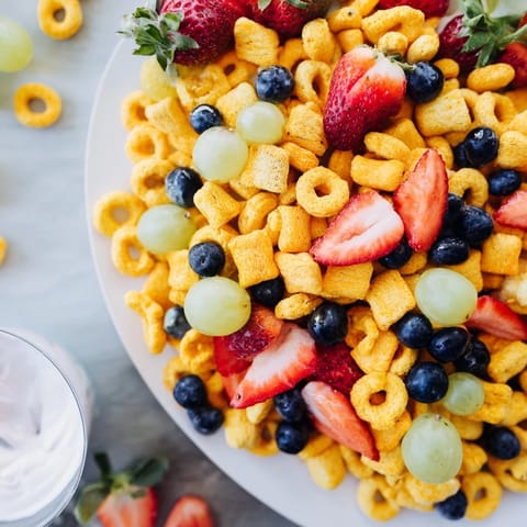 Brightly colored Rainbow Goldfish crackers spilling out next to juicy grapes, berries, and a yogurt dip.