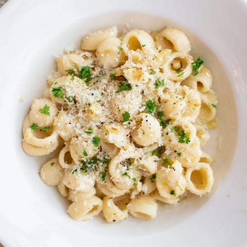 Steaming bowl of ditalini pasta with creamy garlic sauce sprinkled with fresh parsley and cheese.