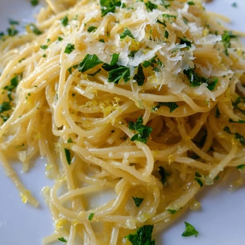 Steaming bowl of Lemon Butter Pasta Light garnished with chopped parsley and grated Parmesan, ready to serve.  