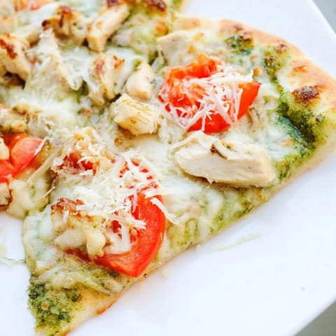 Freshly baked Chicken Pesto Pizza showcases a crispy thin crust topped with juicy chicken, aromatic basil pesto, and golden cheese.  
