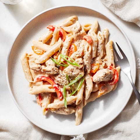A close-up of Sweet Chili Chicken Pasta garnished with fresh green onions, sesame seeds, and cilantro.