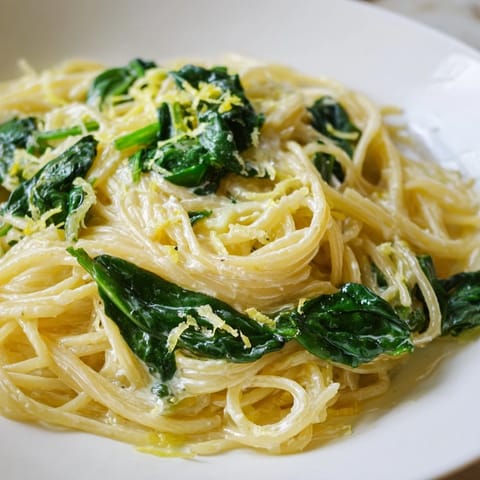 Fork twirls in creamy lemon spinach spaghetti, with steam rising and Parmesan melting over wilted greens.  