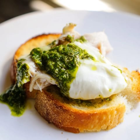 Crispy sourdough toast topped with tender chicken, basil pesto, and creamy burrata, garnished with fresh basil leaves.  