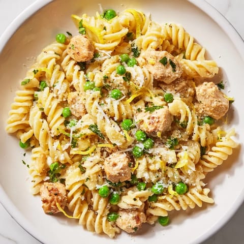 Twirls of pasta in Garlic Butter Chicken & Pea Pasta are coated in a glossy sauce, garnished with fresh parsley and lemon zest.