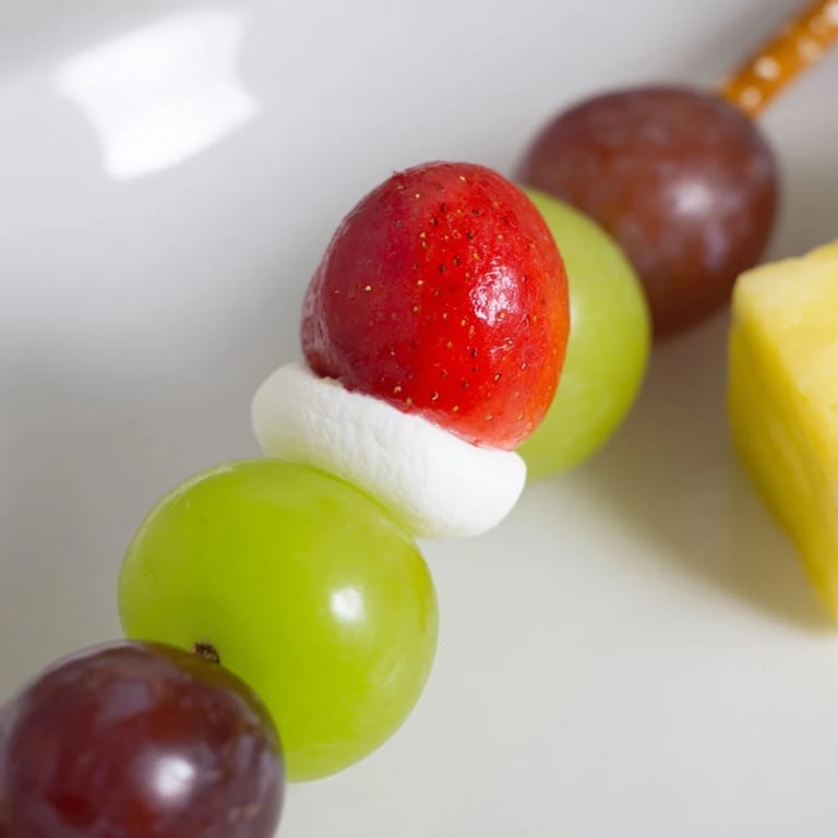 Festive Christmas Light Fruit Skewers showcase bright fruit bulbs on pretzel sticks, ready for a kid-friendly snack.