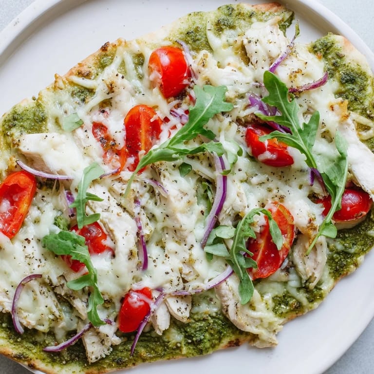 Freshly baked Pesto Chicken Flatbread, a weeknight meal featuring pesto, cheese, and vibrant red tomatoes.