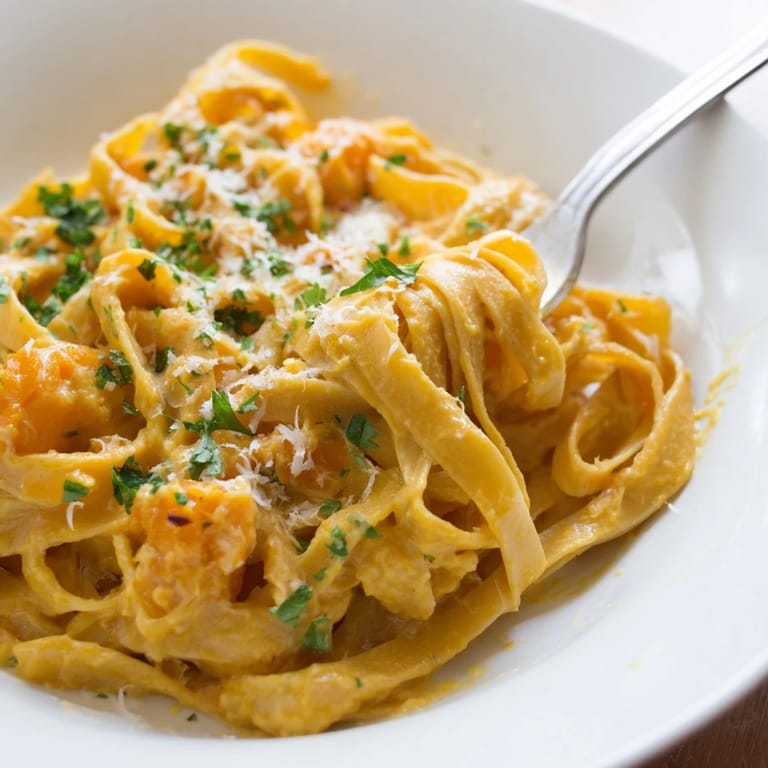 A close-up view of creamy Butternut Squash Pasta tossed with fettuccine in a velvety orange sauce, garnished with fresh parsley and grated Parmesan.