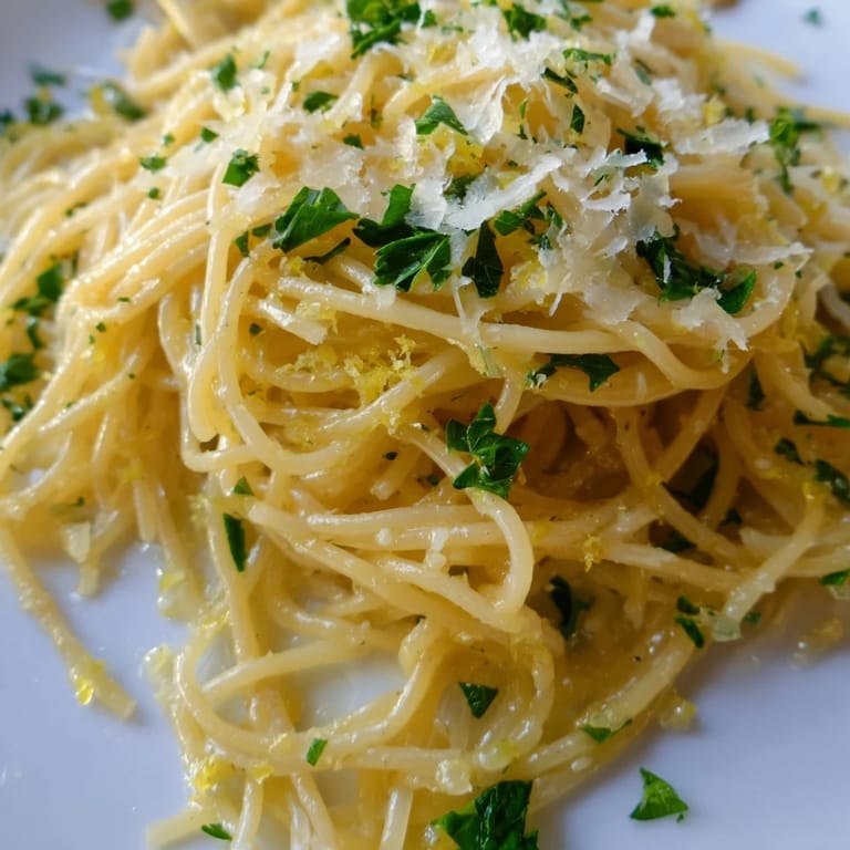 Steaming bowl of Lemon Butter Pasta Light garnished with chopped parsley and grated Parmesan, ready to serve.  
