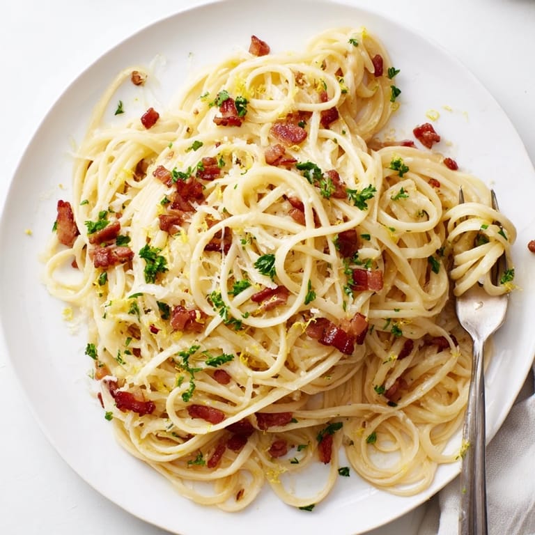 Hot skillet of Crispy Bacon Linguine next to golden, crisp bacon pieces and a wedge of lemon.