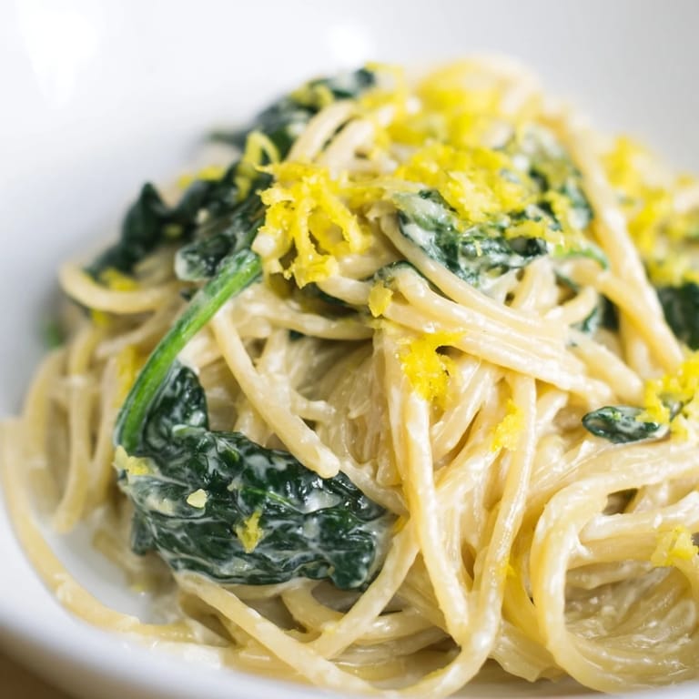 Al dente spaghetti glistens in a silky lemon cream sauce, flecked with bright spinach and zest.  