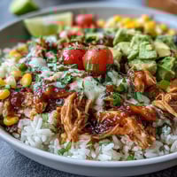 A colorful bowl of salsa chicken served over rice with black beans, corn, and fresh avocado slices for a healthy meal.  